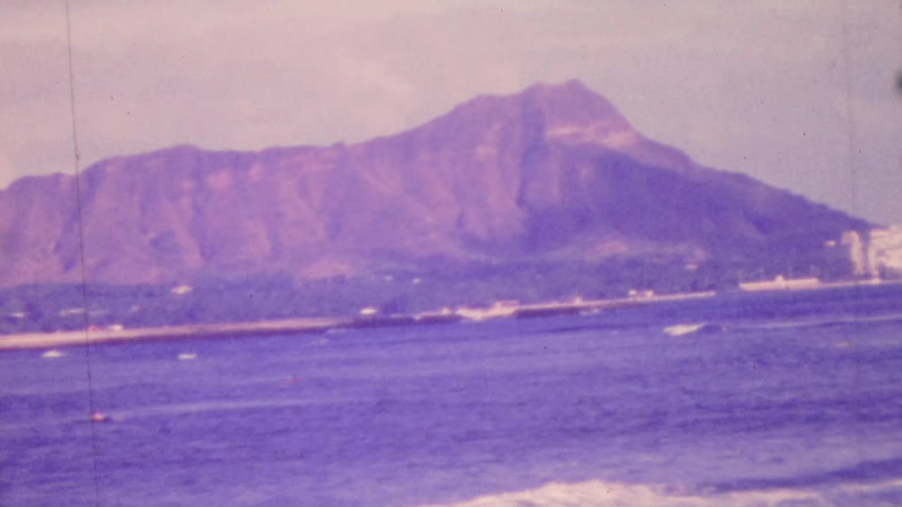 1964 Honolulu view across the Pacific toward Diamond Head, with a low coastal strip and distant buildings visible in soft 8mm color.