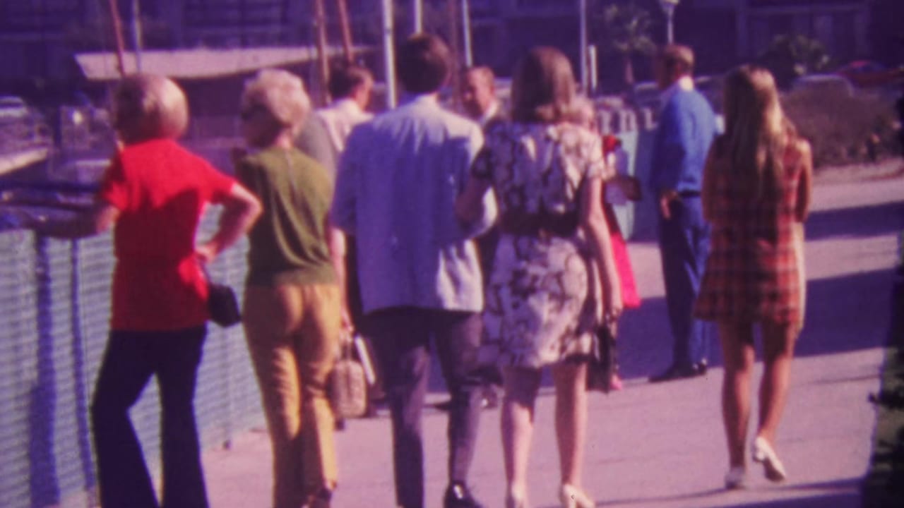 Group of adults walking away from the camera beside blue railings and docked boats.