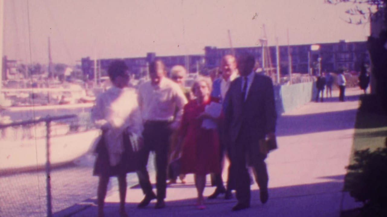 Group of adults walking on a marina dock with sailboats and water in the background.