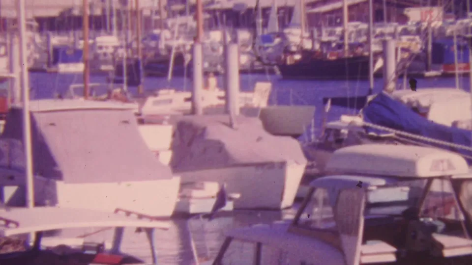 1964 Honolulu marina frame with a small cabin boat in the foreground, covered sailboats, white pilings, many masts, and still harbor water.