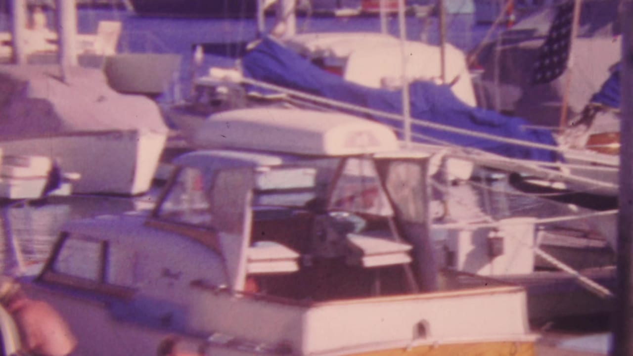 Cabin cruiser in the foreground with sailboats and blue canvas covers behind it.