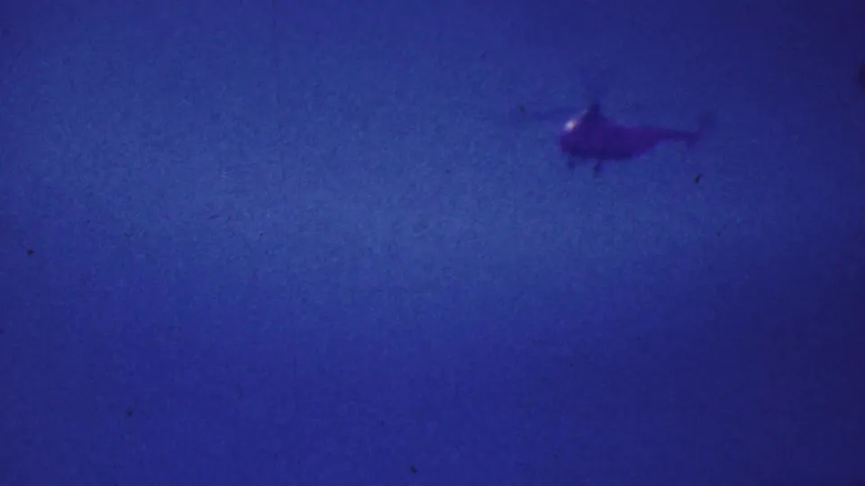 Distant helicopter filmed against a blue sky, continuing the 1964 Palm Springs home-movie cutaway from beach activity to aviation.