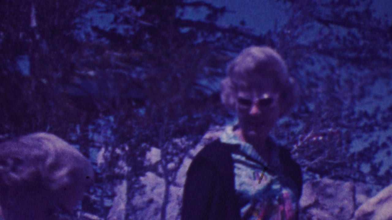 Two older women partially visible among trees and rocks, with one wearing sunglasses and a patterned top.