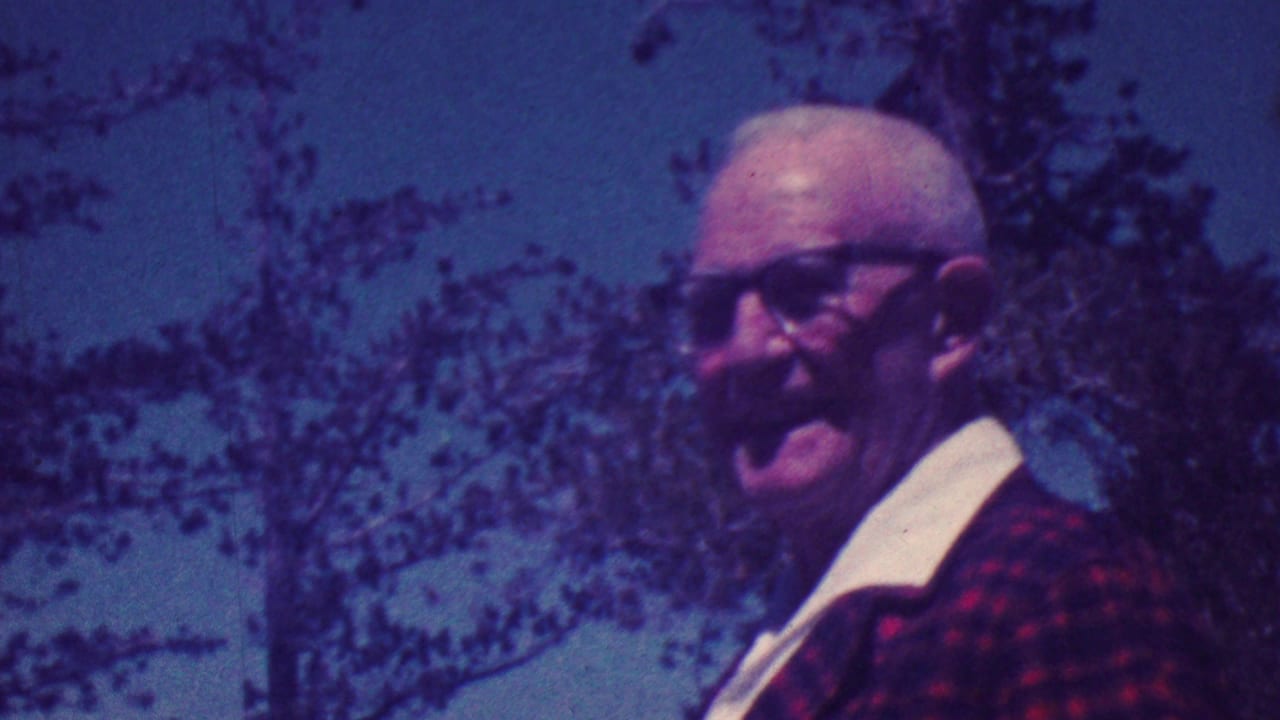 Older man with glasses appears in close outdoor framing against trees.