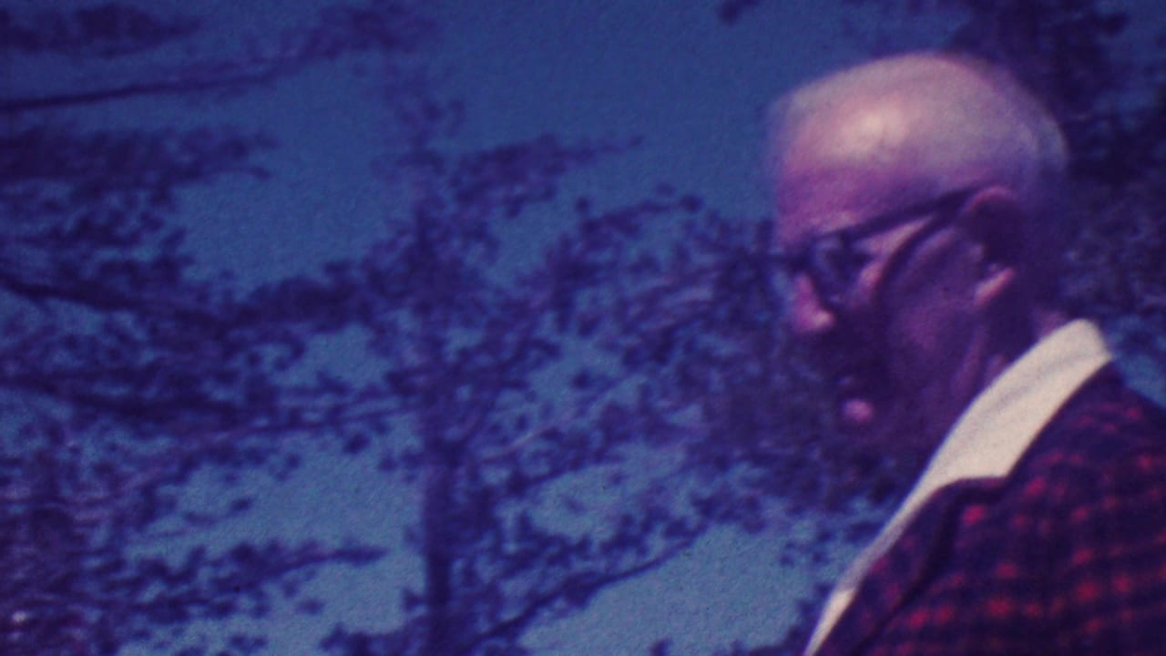 Elderly man in a red plaid jacket and glasses appears at an outdoor memorial plaque site in Palm Springs, California, in 1964 home-movie footage.
