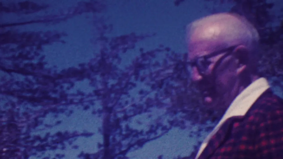 Elderly man in a red plaid jacket and glasses appears at an outdoor memorial plaque site in Palm Springs, California, in 1964 home-movie footage.