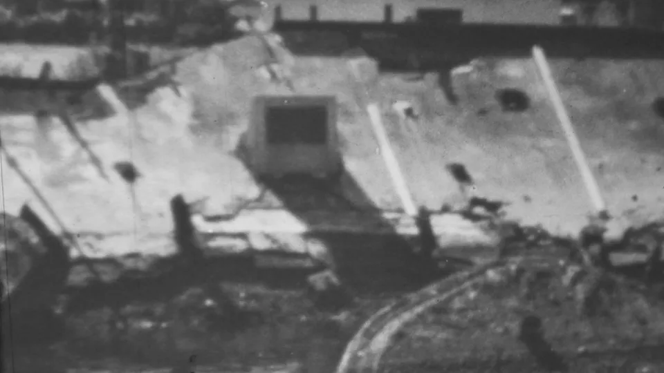 Wider 1962 Honolulu/Pearl Harbor-area 8mm view showing floodwater around a damaged structure, debris, and bare tree branches in soft black-and-white focus.