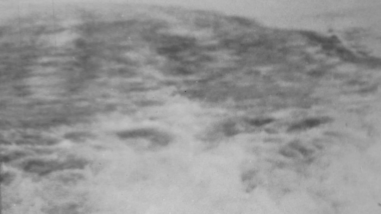 Black-and-white 1962 8mm frame from the Pearl Harbor, Honolulu area showing breaking surf and a blurred shoreline beyond the water.