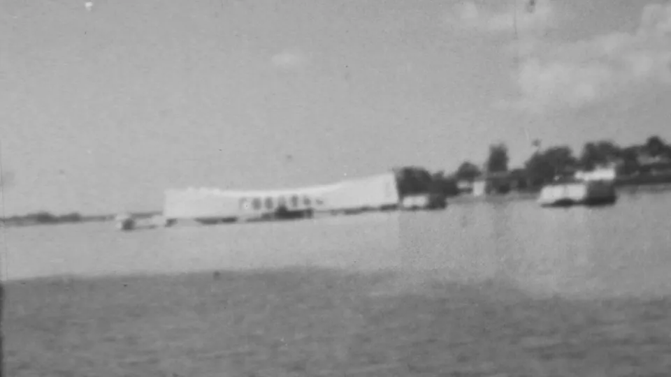 Final frame holds on the Pearl Harbor memorial area in Honolulu, with the white structure, nearby boats, and shoreline seen through soft black-and-white 8mm texture.