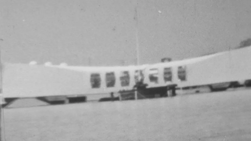 Closer 1962 black-and-white home-movie view of the USS Arizona Memorial at Pearl Harbor, with its white curved form and dark window bays visible over the water.