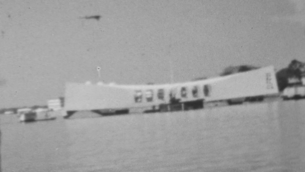 Soft black-and-white 1962 8mm frame showing the Pearl Harbor memorial area in Honolulu from across the water during a moving pass-by.