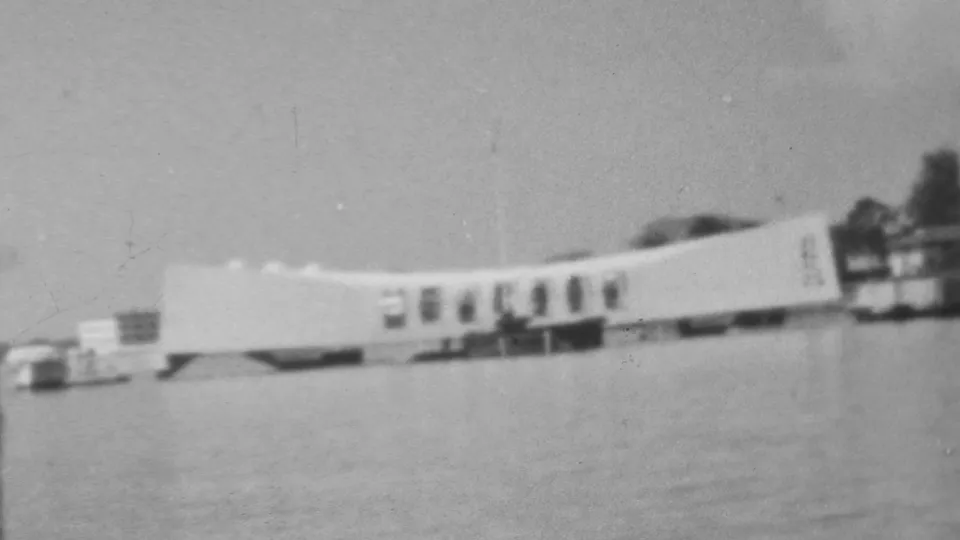 1962 8mm frame showing the Pearl Harbor memorial area from a passing viewpoint, with the long white structure softened by motion and film grain.