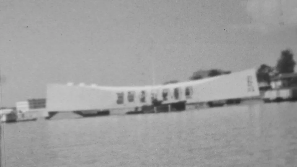 Final black-and-white 8mm frame of the Pearl Harbor memorial view in Honolulu, with the white over-water structure receding toward dark shoreline trees.