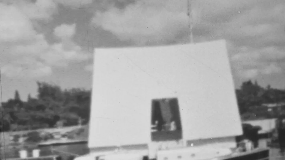Black-and-white 8mm frame from the 1962 Pearl Harbor memorial clip, showing the white structure filling much of the view above harbor water.