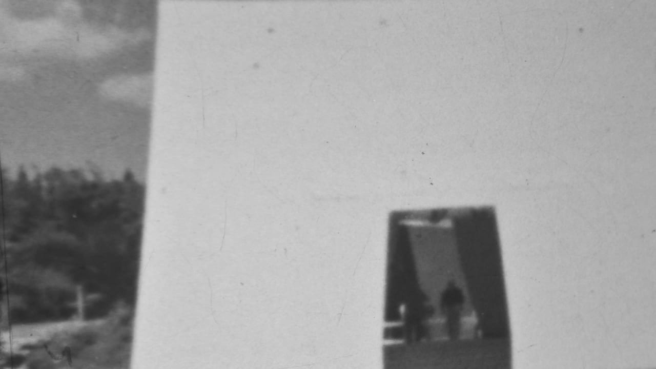 Bright concrete wall with a dark recessed doorway and two small silhouetted figures.