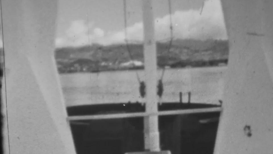 Visitor-shot 8mm view from a Pearl Harbor-area structure looking through a window or opening toward water, distant mountains, and a clouded sky.