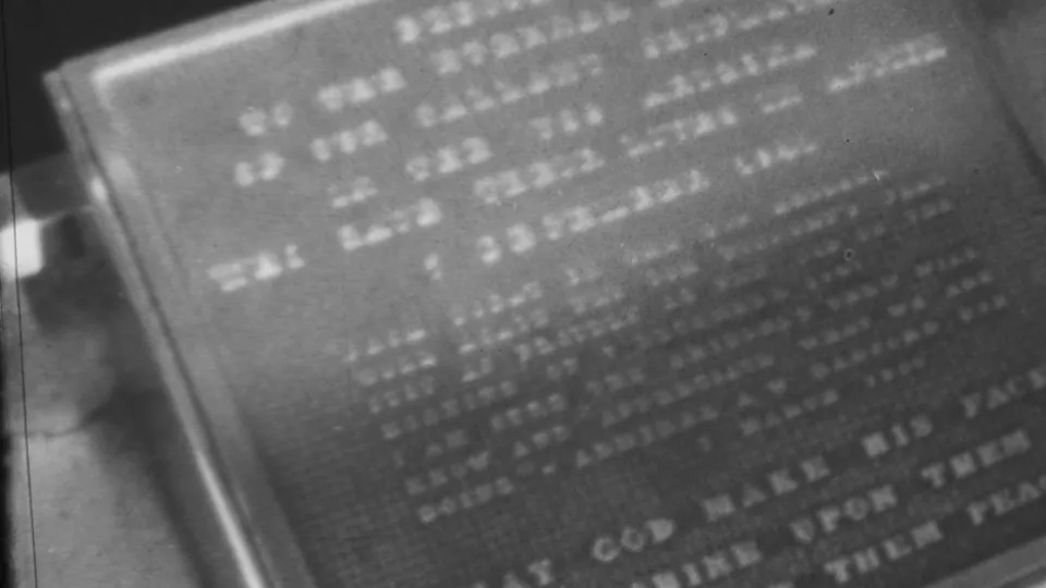 Close 1962 8mm frame of a weathered engraved plaque at the Honolulu monument site, with text visible but too soft to identify reliably from the still.