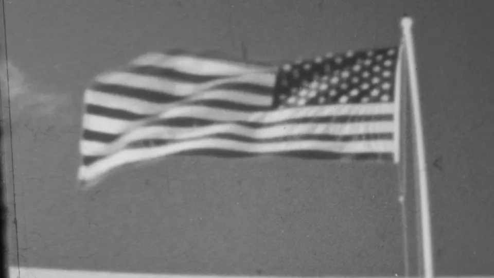 Black-and-white 8mm frame of an American flag waving on a pole during the Pearl Harbor, Hawaii visitor sequence.
