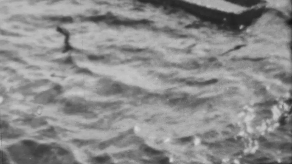 Final frame showing textured harbor water beneath the partially visible concrete tank edge, with soft focus and visible 8mm film wear.