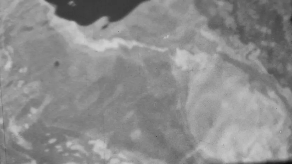 Black-and-white 8mm frame from the Pearl Harbor-attributed clip showing shallow moving water, a dark wet shoreline edge, and soft pale surface patterns.