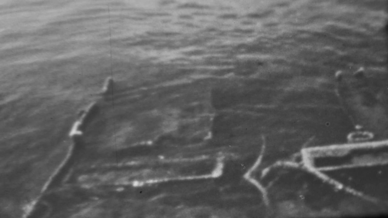 Black-and-white 1962 Pearl Harbor footage showing rippled water and indistinct submerged shapes that may be ship or equipment remains.