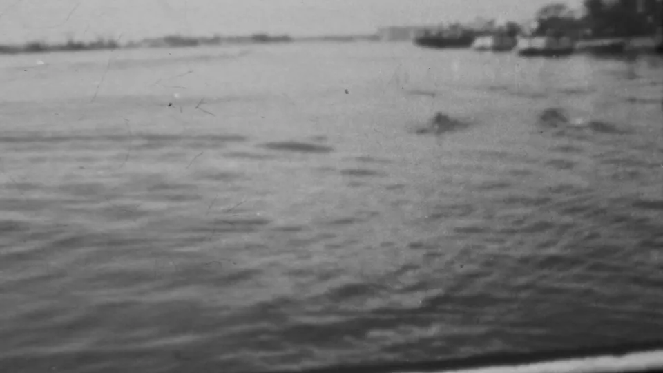 A 1962 Honolulu-area harbor view shows water in the foreground, a low distant shoreline, and indistinct craft or shoreline structures softened by 8mm focus.
