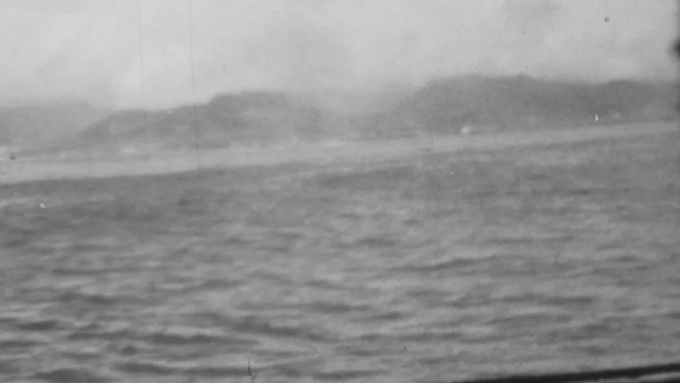 Wider 1962 Pearl Harbor-area view over rippled water toward a hazy shoreline, following the submarine shots in the same black-and-white 8mm clip.