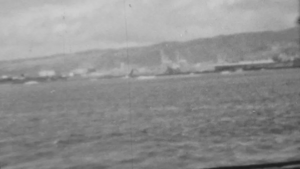 The 1962 shipboard view continues along Pearl Harbor, with rippled water below and a distant waterfront partly obscured by haze or smoke.