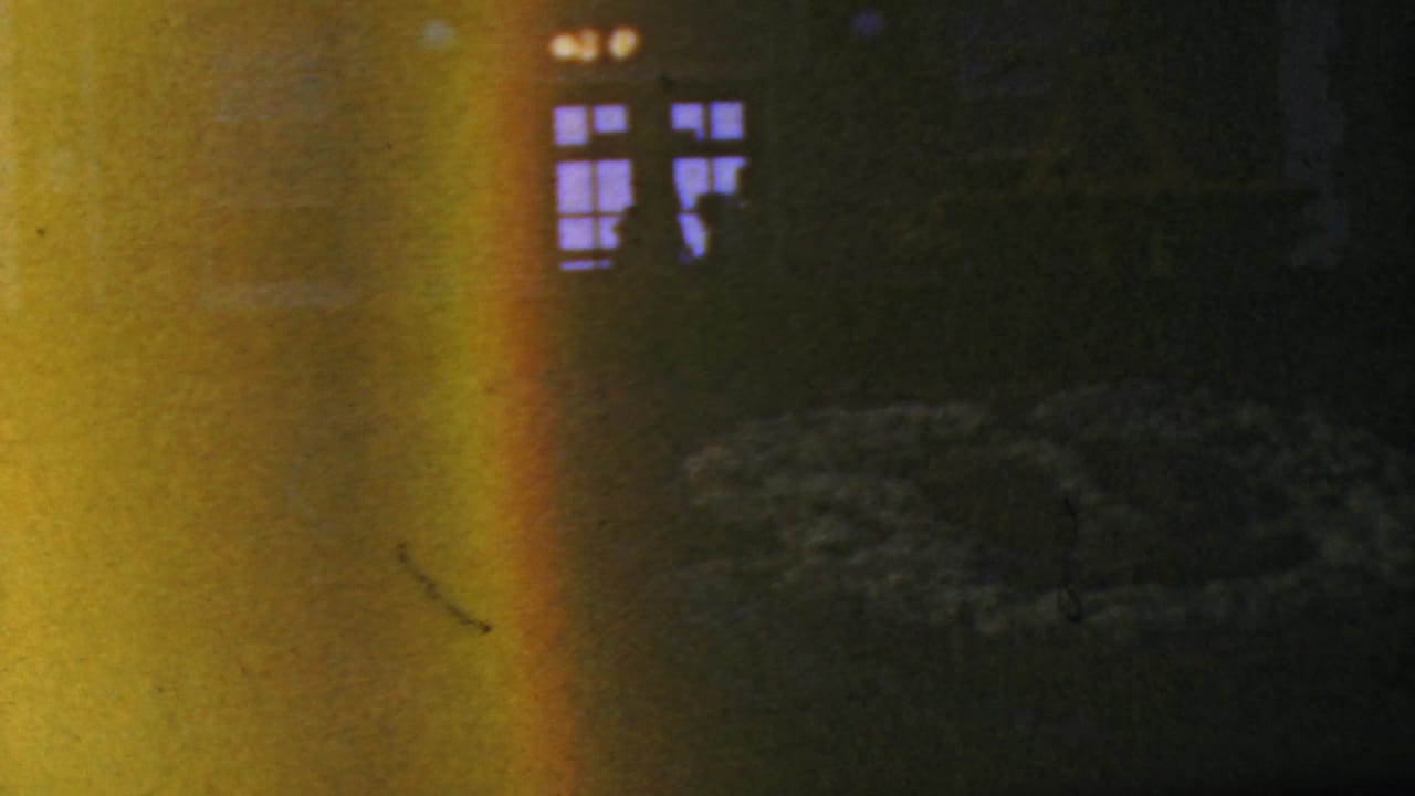 Dark entrance facade with glowing windows and a broad yellow film flare.
