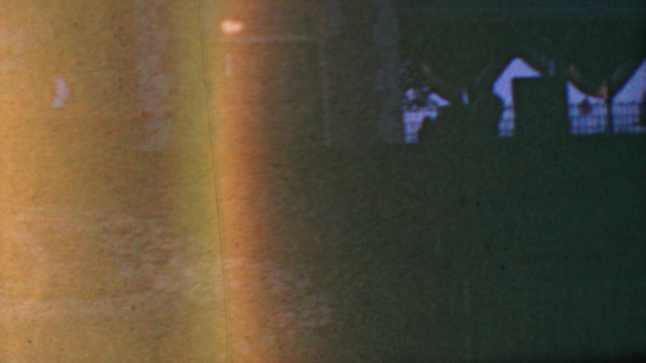1964 Anaheim home-movie frame with green lawn, dark silhouettes, distant white structures, and heavy color shift across the 8mm image.