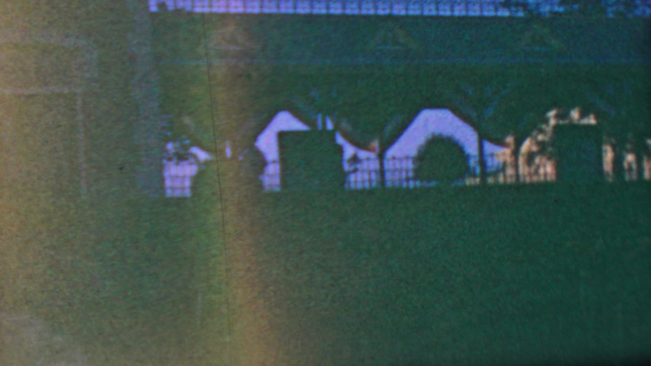 Distant park structures behind a lawn with dark foliage and a fence line.