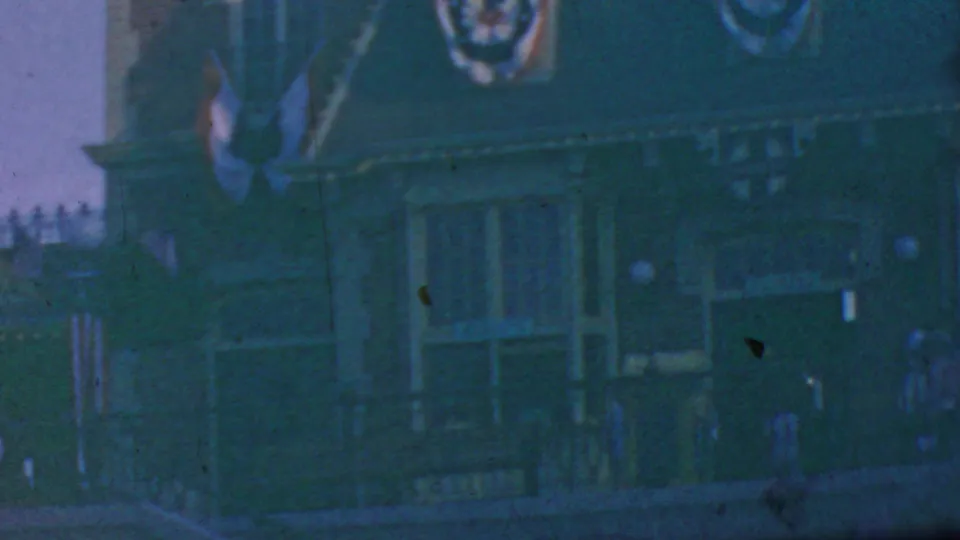 1964 Anaheim visitor-shot frame showing a building facade decorated with American flags and banners, with small distant people near the lower edge.
