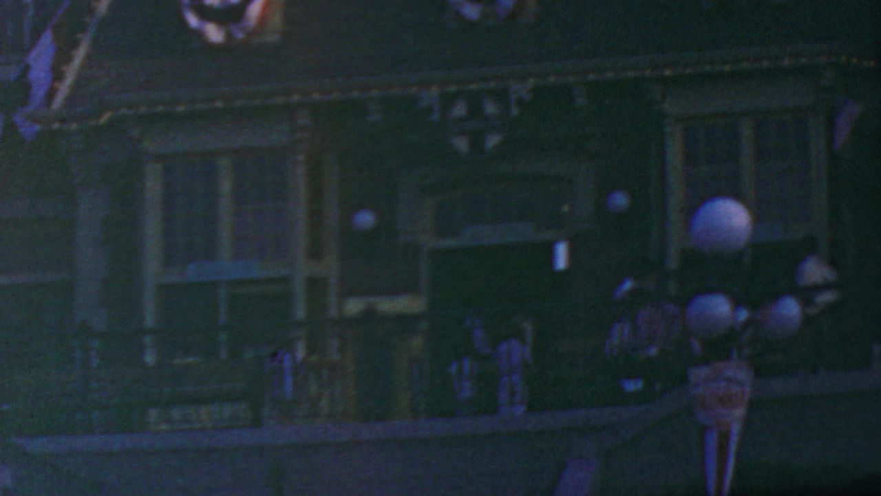 Dim parade-route view with bunting, lamps, and uniformed figures near the building facade.