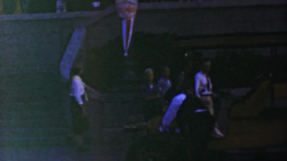 1964 Anaheim Disneyland home-movie frame showing adults in low light near a railing and raised event structure, with heavy grain and color shift.