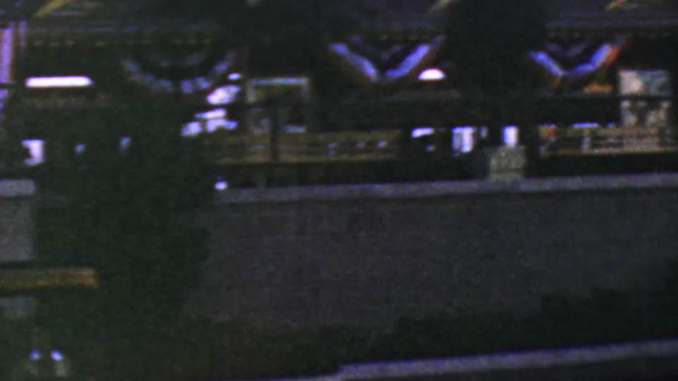 1964 Anaheim Disneyland home-movie frame showing a dim ceremony or parade area with railings, decorative shapes, and distant people under nighttime lighting.