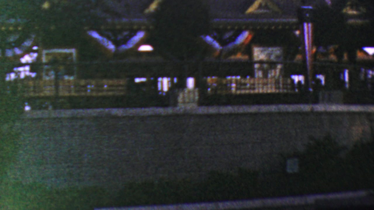 1964 Anaheim Disneyland home-movie frame showing a dark park structure with railings, low lamps, trees, and a foreground wall in soft night exposure.