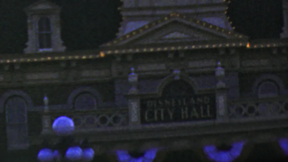 1964 Anaheim frame showing the Disneyland City Hall sign on the facade, with lit roof trim, arched lower windows, decorative railings, and globe lamps near the bottom edge.
