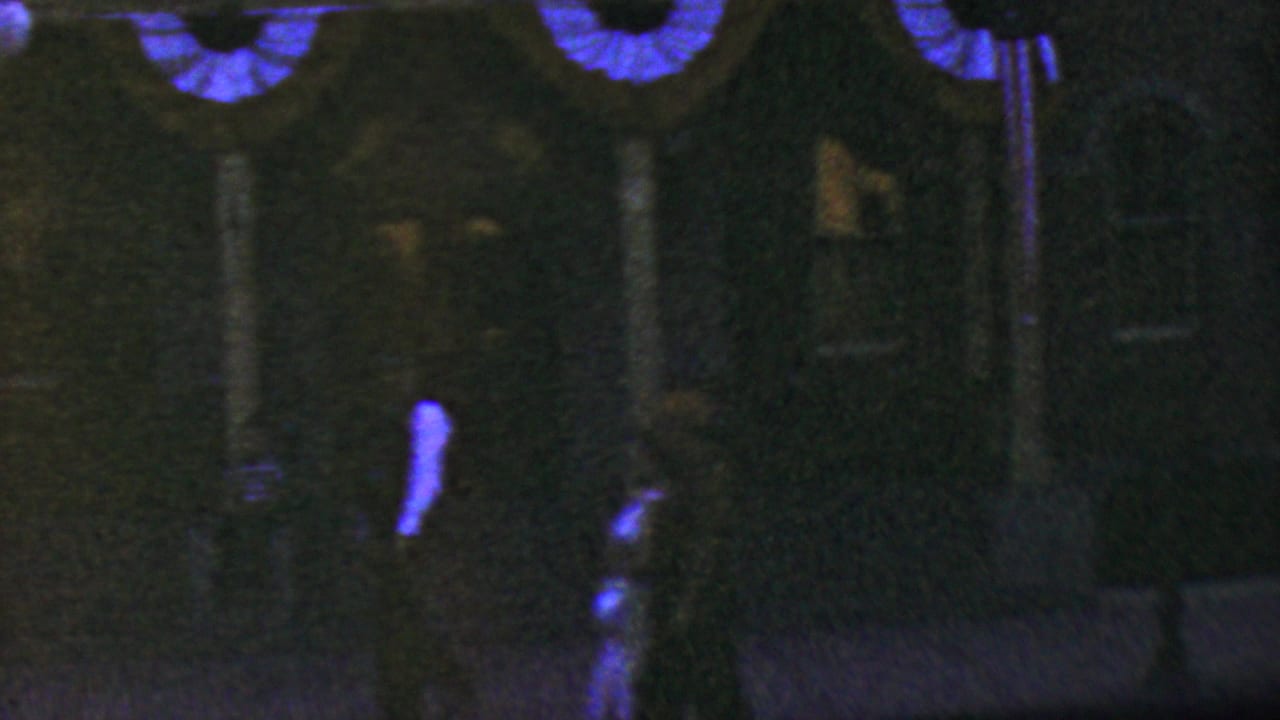 1964 Anaheim amusement-park frame with a dark entrance-like building, blue swags overhead, and partially visible visitors crossing the foreground.