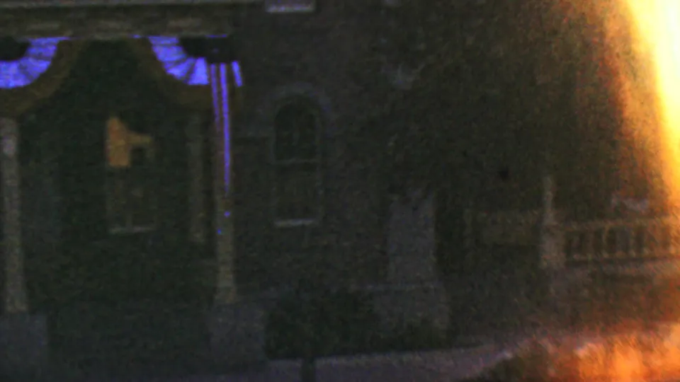 Low-light 1964 Disneyland frame showing a dark architectural facade with columns and windows, partly washed by orange film flare.