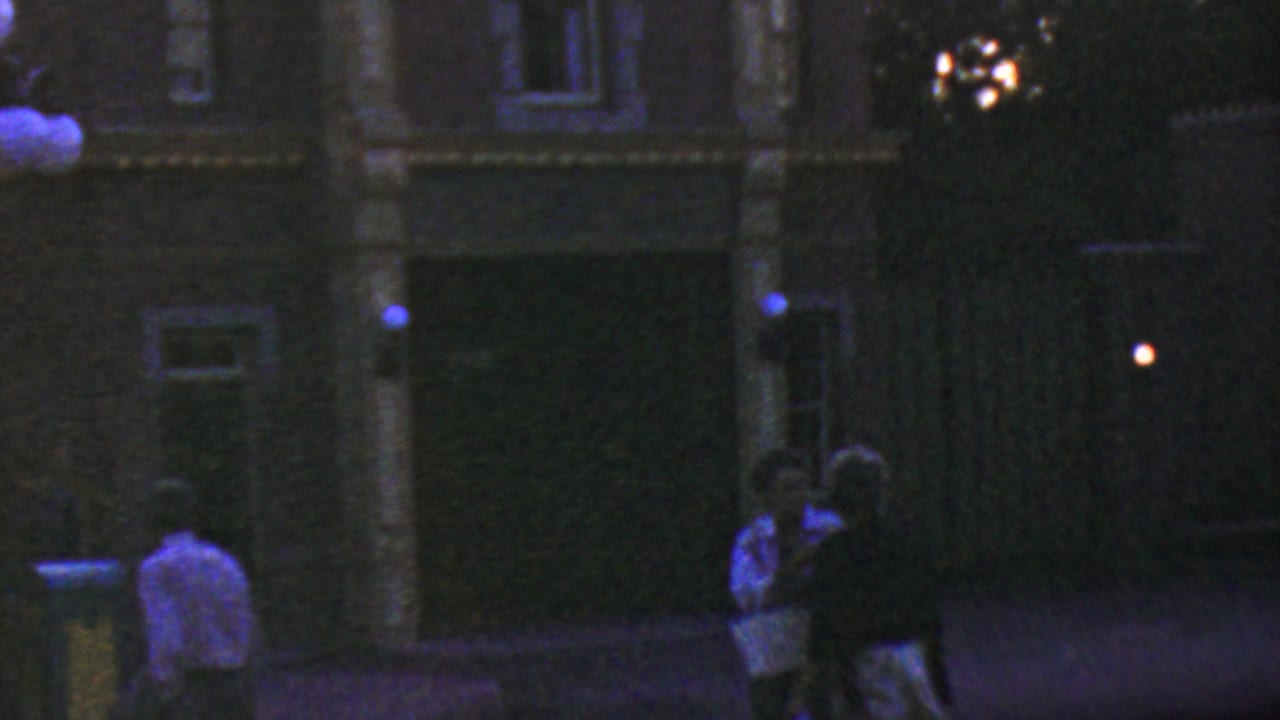 Nighttime building front with pedestrians in shadow and several round lamps near the upper left.