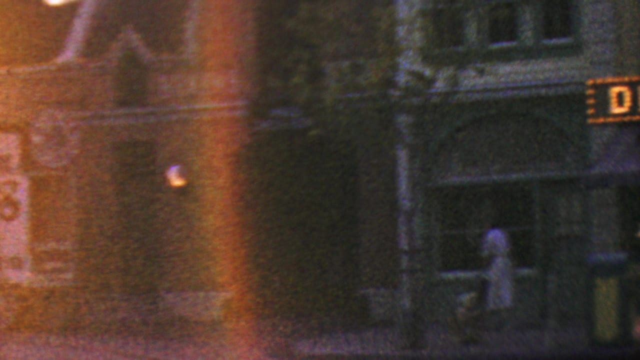 1964 Anaheim Disneyland night footage shows a dim street scene with part of the illuminated Disneyland sign, storefront windows, and visitors walking past.