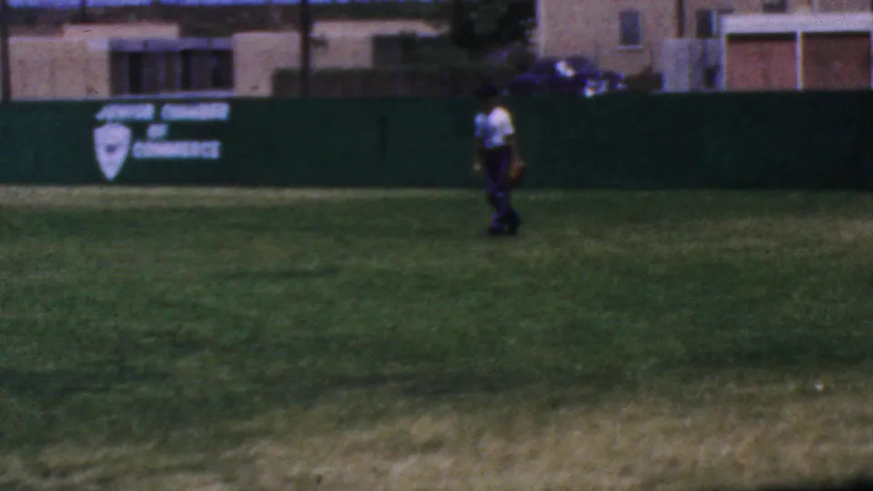 End frame of the 1964 Anaheim Disneyland home movie showing a distant figure walking across the baseball outfield with green wall signage behind them.