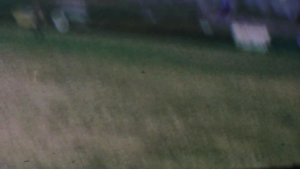 Handheld 8mm frame showing a green playing field with soft focus, color shift, and indistinct background structures from the Anaheim baseball scene.