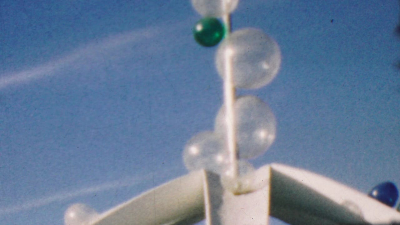 1964 Disneyland home-movie frame showing a white ornamental pole with clear bubble-like globes and a green sphere, filmed against a bright blue sky.