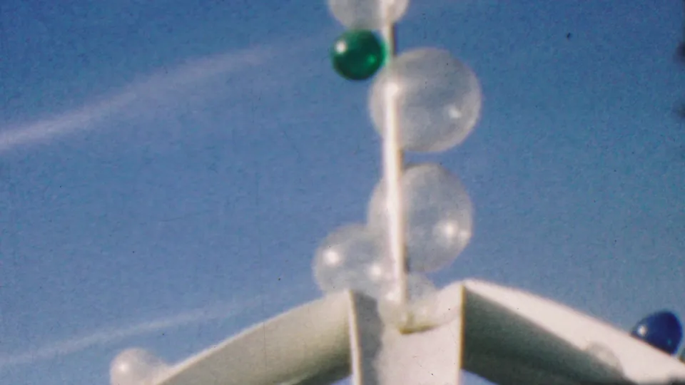 1964 Disneyland home-movie frame showing a white ornamental pole with clear bubble-like globes and a green sphere, filmed against a bright blue sky.