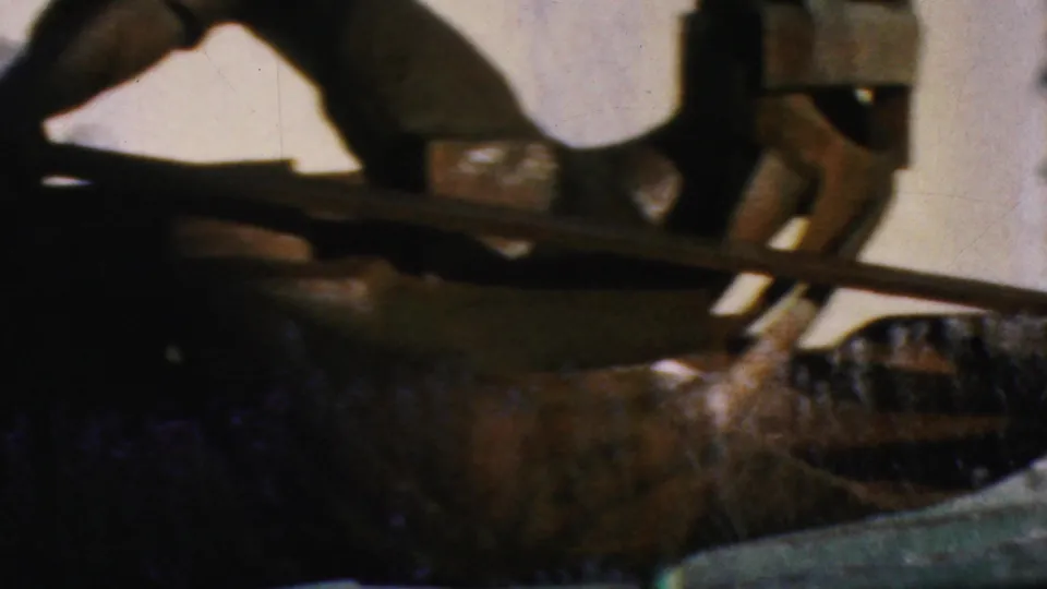 Final 1964 8mm frame showing a close, soft-focused view of the metal human-like sculpture with limbs, rod, fountain basin, and pale background.