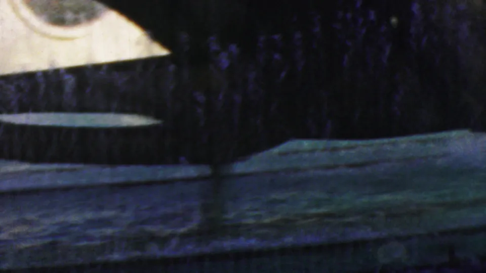 Final 1964 Anaheim frame with dark silhouetted structure, pale oval surfaces, water or fountain foreground and heavy Super 8 grain.