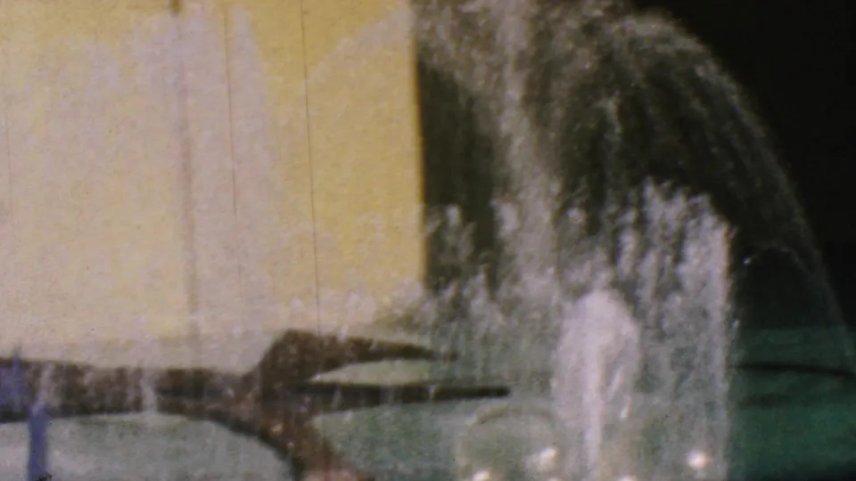 1964 Anaheim Disneyland home-movie frame showing fountain spray, a curved basin edge, yellow wall panels, and a dark overhead water feature.