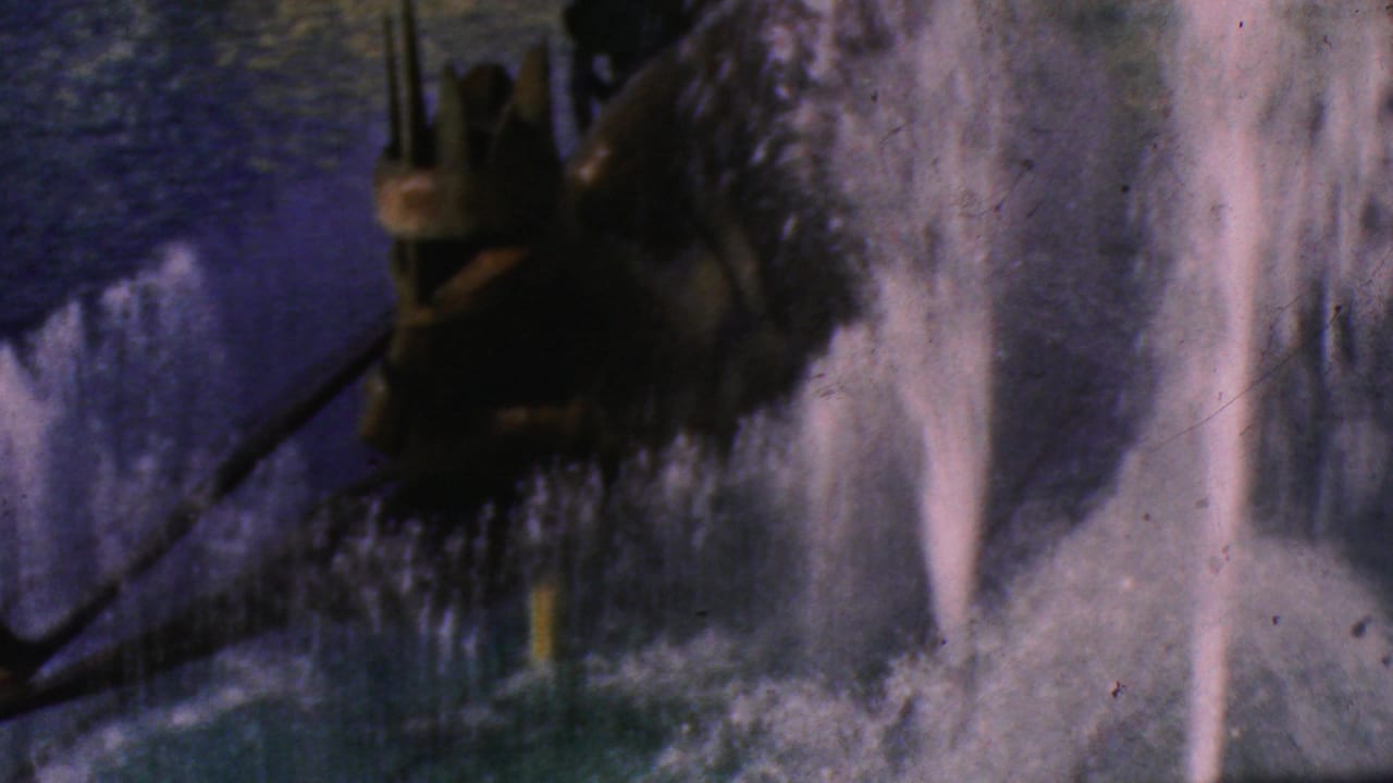 1964 8mm Disneyland home-movie frame showing cascading fountain spray near a dark sculptural element, with soft color and grain from the original film.