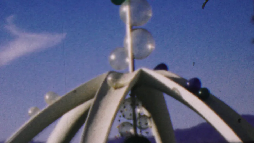 Close visitor view of the Disneyland outdoor sculpture, with white metal arms, stacked clear glass bubbles, and a blue sky backdrop in the supplied 1964 Anaheim context.